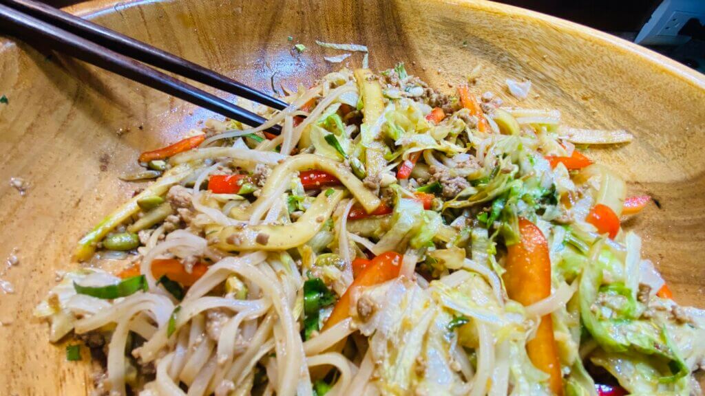 Spicy beef noodles in a wooden bowl, garnished with vegetables, served with chopsticks for an authentic dining experience.